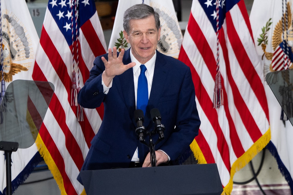 North Carolina Governor Roy Cooper stands behind a lectern waving.