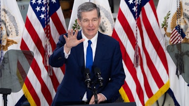 North Carolina Governor Roy Cooper stands behind a lectern waving.