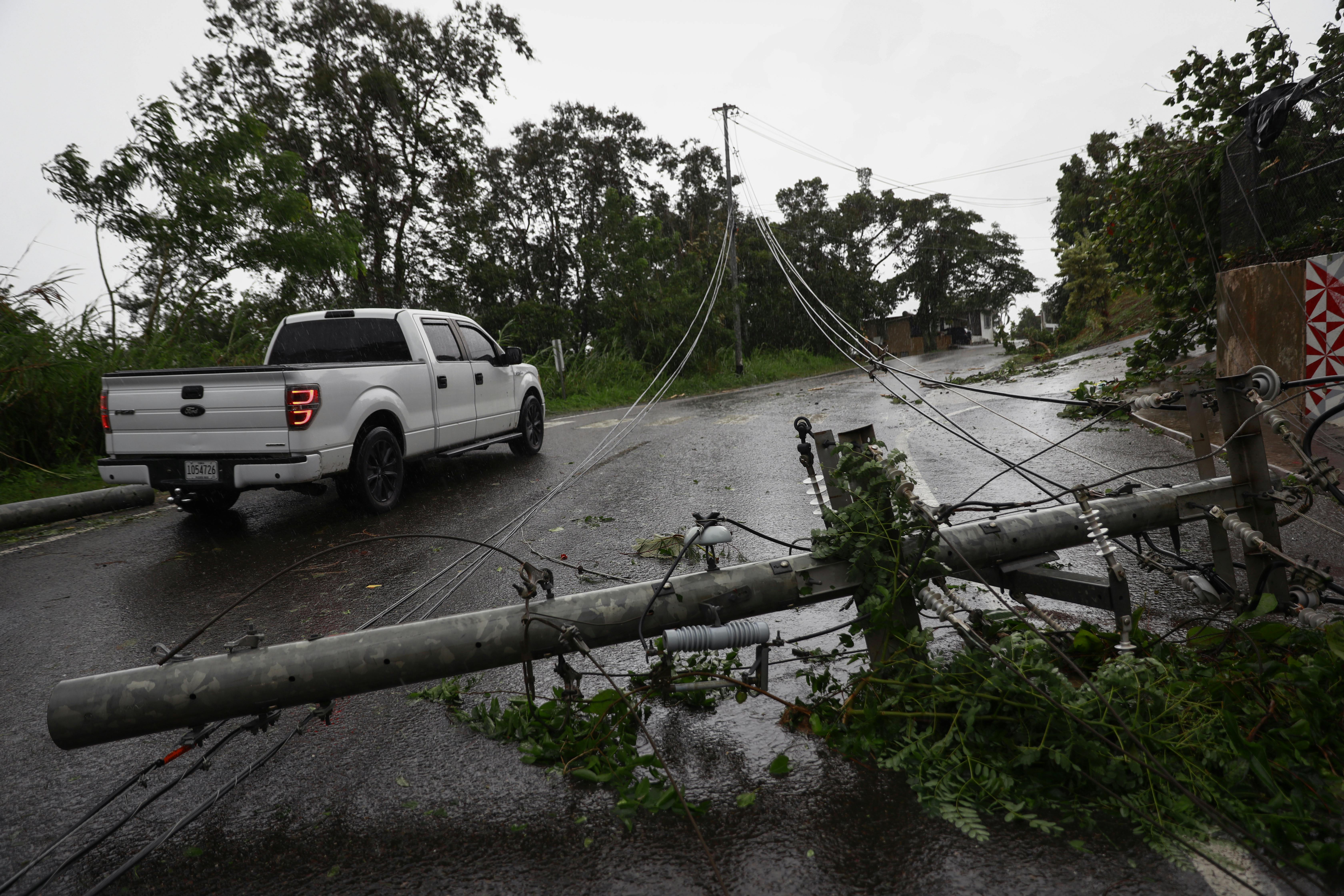 A pickup truck drives next to downed power lines.