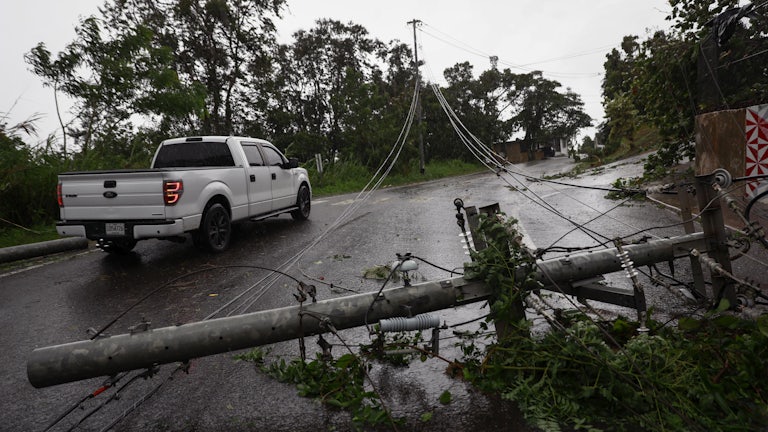 A pickup truck drives next to downed power lines.