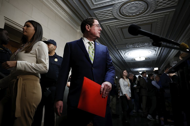 Representative Mike Flood looks behind him as he walks through the Capitol, a red folder in his hand and reporters lining the hallway.
