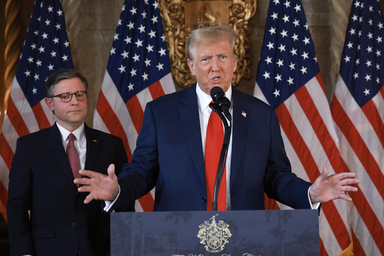 Mike Johnson stands behind Donald Trump as he speaks at a podium