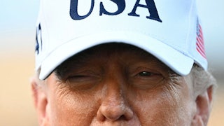 President Trump is seen from the nose up in a white, USA cap.