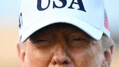 President Trump is seen from the nose up in a white, USA cap.