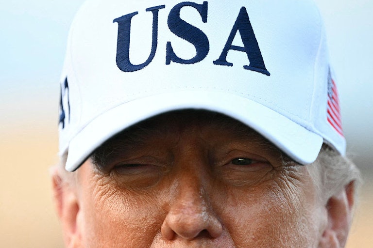 President Trump is seen from the nose up in a white, USA cap.