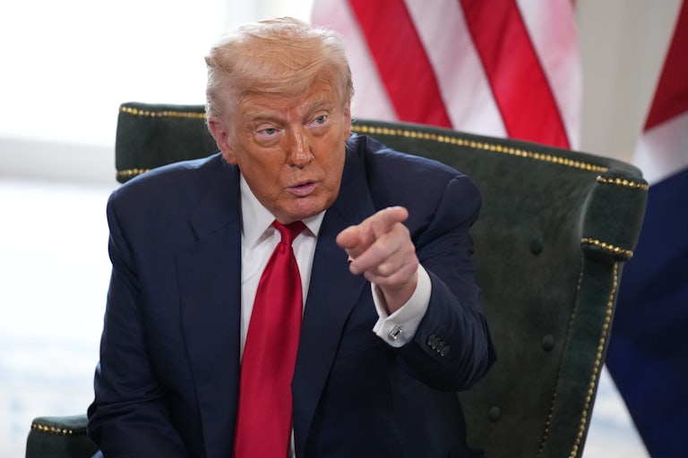 Donald Trump sits on a chair and points as he speaks