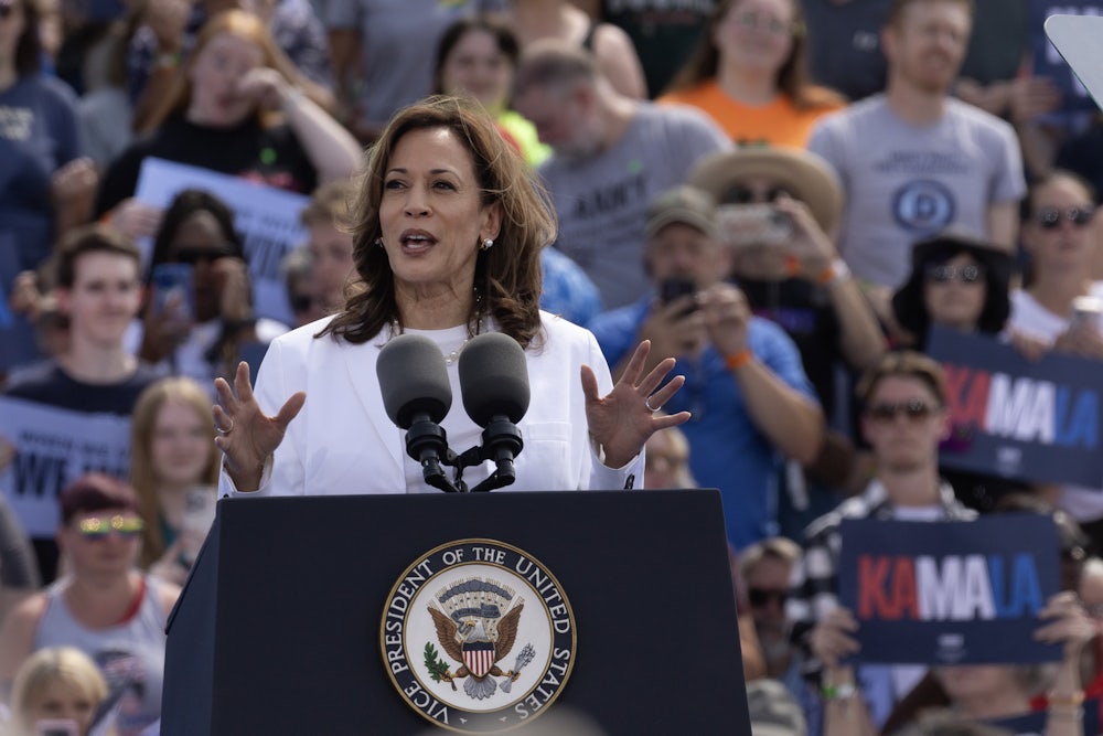 Kamala Harris, dressed in all white, speaks at a podium with supporters behind her.