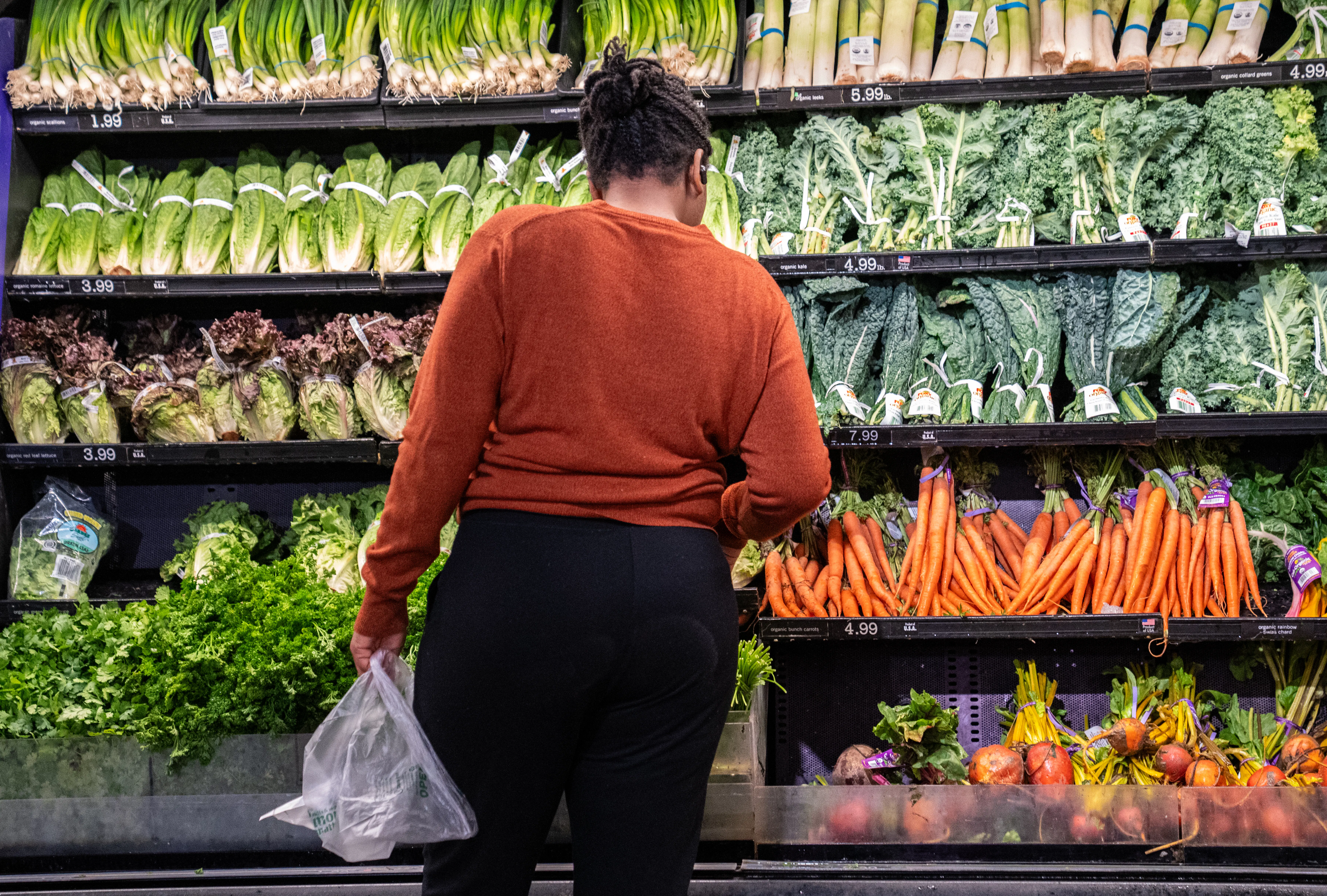 A woman stands in front of the vegetables in a grocery store.