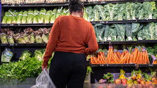 A woman stands in front of the vegetables in a grocery store.