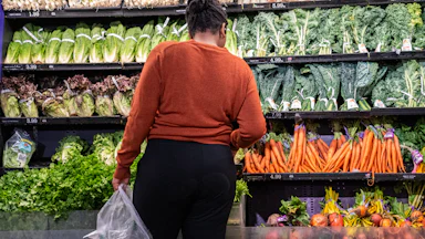 A woman stands in front of the vegetables in a grocery store.