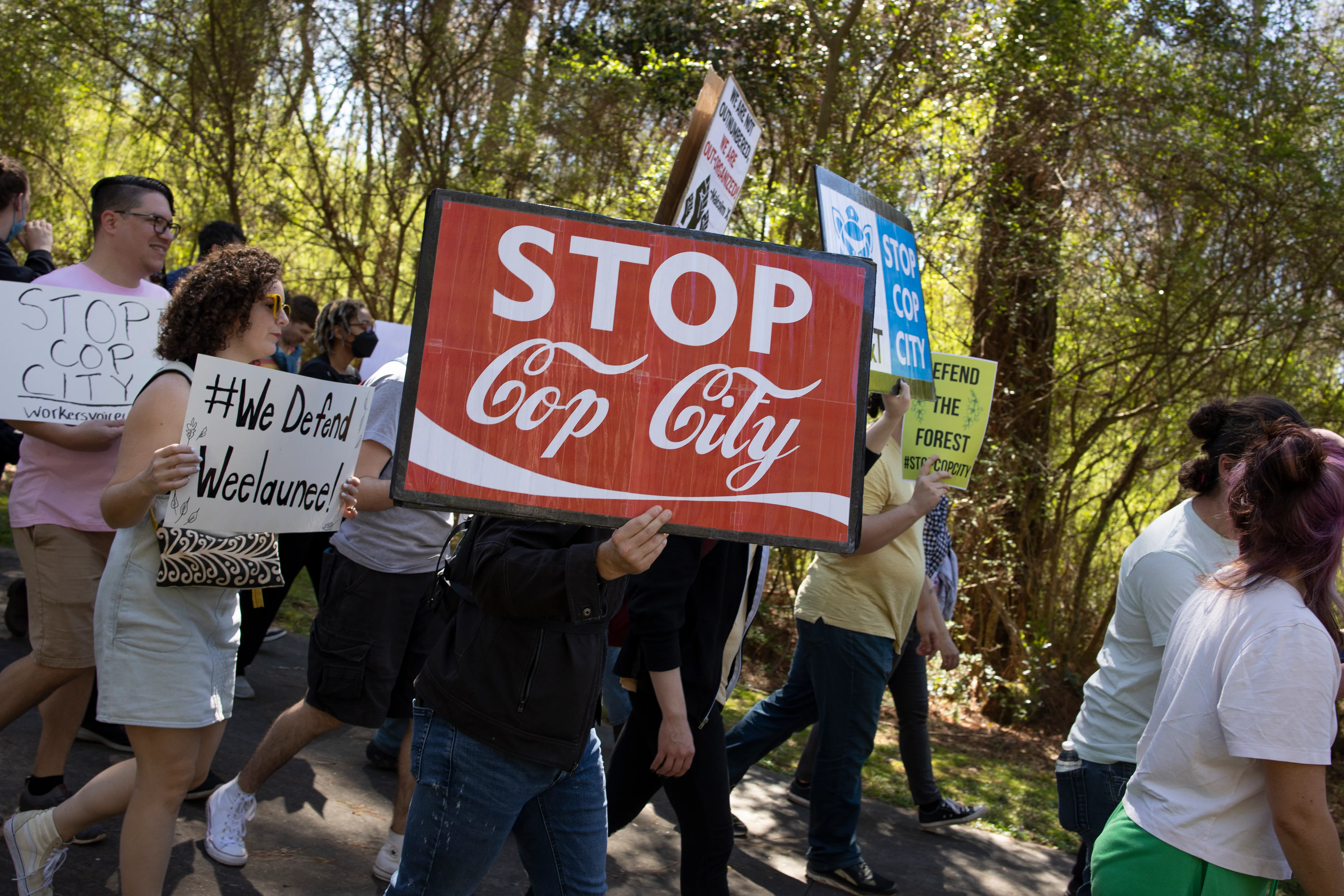 anti-Cop City demonstrators hold a sign reading "stop cop city" in the coca-cola font