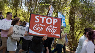 anti-Cop City demonstrators hold a sign reading "stop cop city" in the coca-cola font