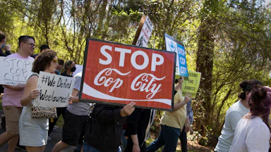 anti-Cop City demonstrators hold a sign reading "stop cop city" in the coca-cola font