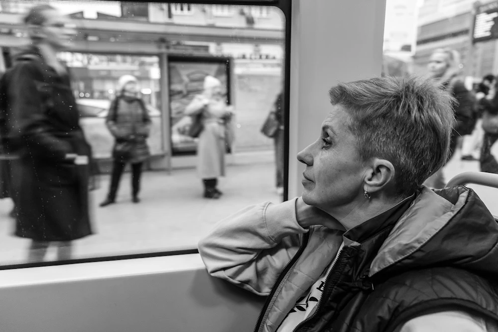 A black and white photograph of Marta Pazdej, a Ukrainian refugee from Lviv, looking out the window at blurry Polish citizens while taking the tram to her boxing class in Warsaw, Poland.