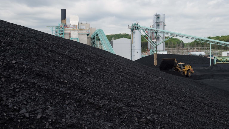 A front-end loader dumps more coal on a giant hill of coal.