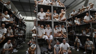 Inmates sit stacked on bunk beds in a massive jail cell.
