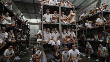 Inmates sit stacked on bunk beds in a massive jail cell.