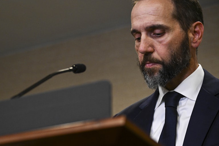 Special counsel Jack Smith looks down while standing at a podium