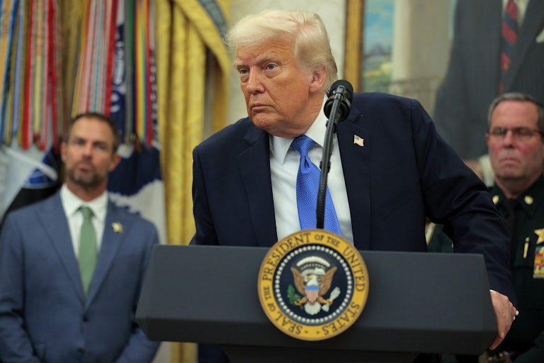 Donald Trump leans forward while standing at the presidential podium in the White House.