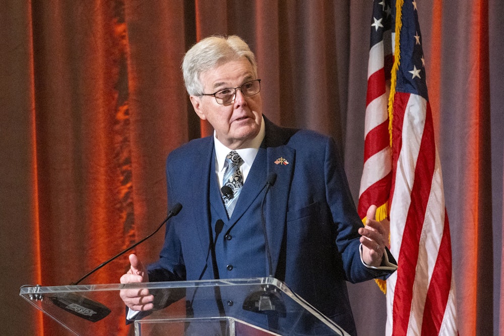 Dan Patrick gesticulates while standing at a lectern.