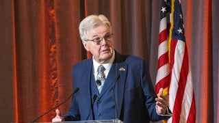 Dan Patrick gesticulates while standing at a lectern.