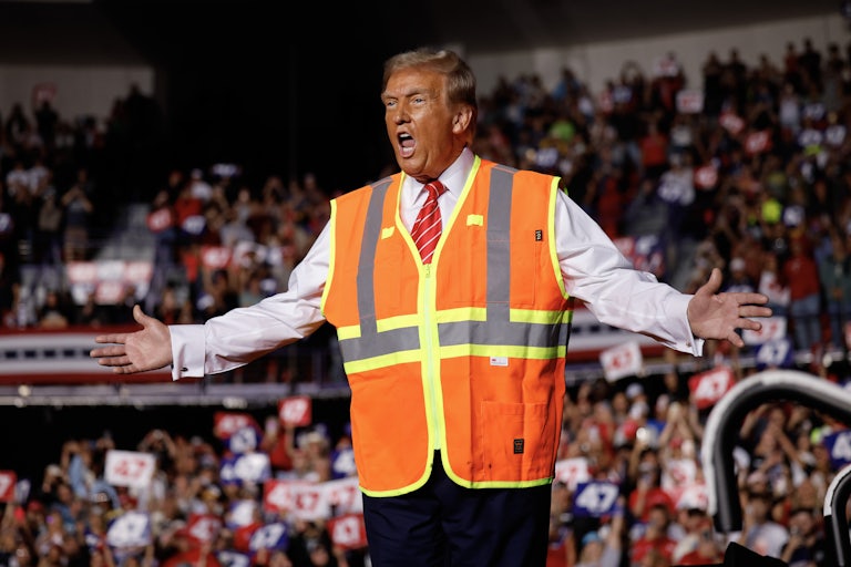 Donald Trump holds his arms out and yells while wearing an orange safety vest at a campaign rally