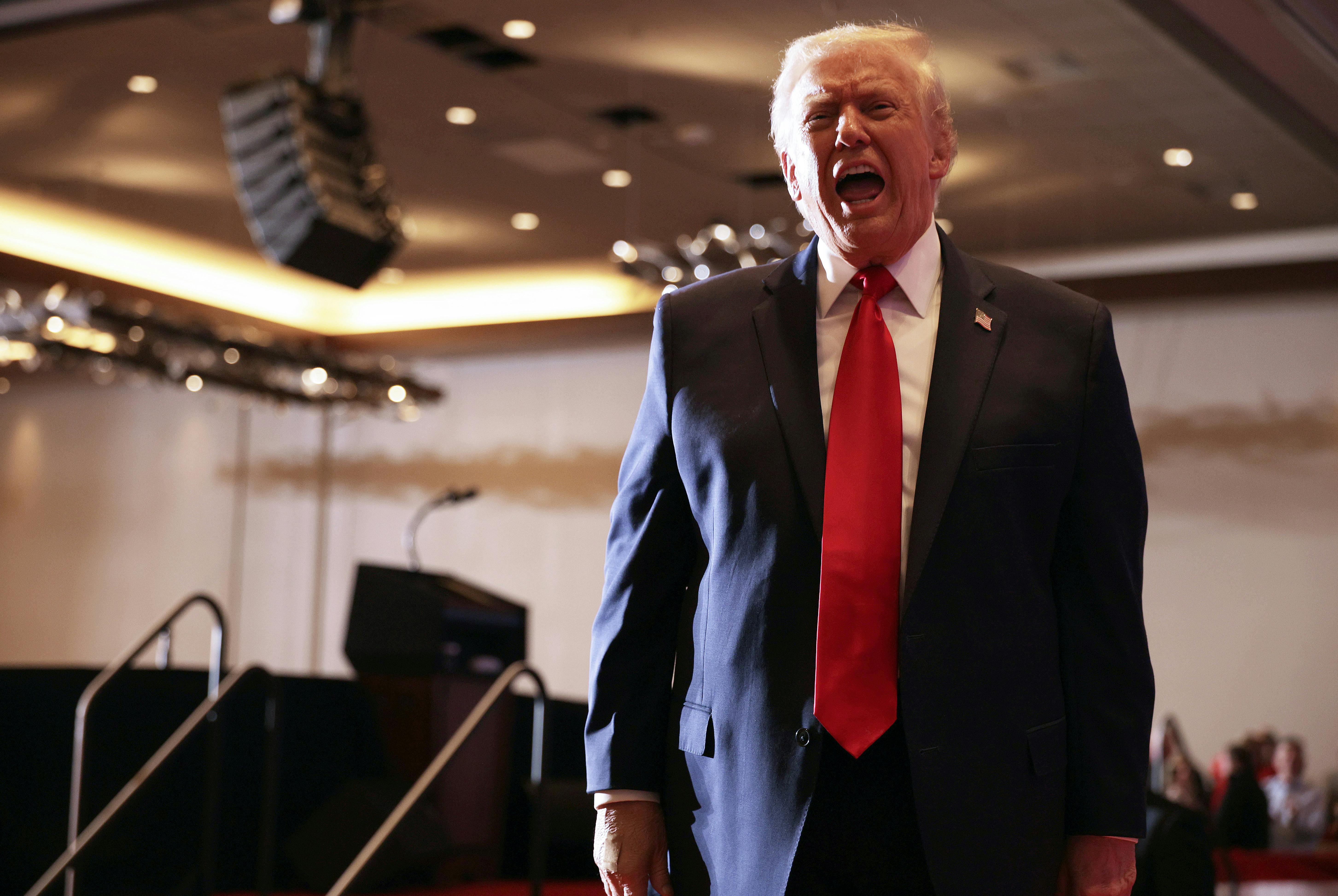 Donald Trump opens his mouth wide and speaks after leaving the stage at an event