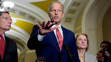 Senate Majority Leader John Thune speaks at a lectern in the Capitol alongside Senate Majority Whip John Barrasso and Senatory Shelley Moore Capito.