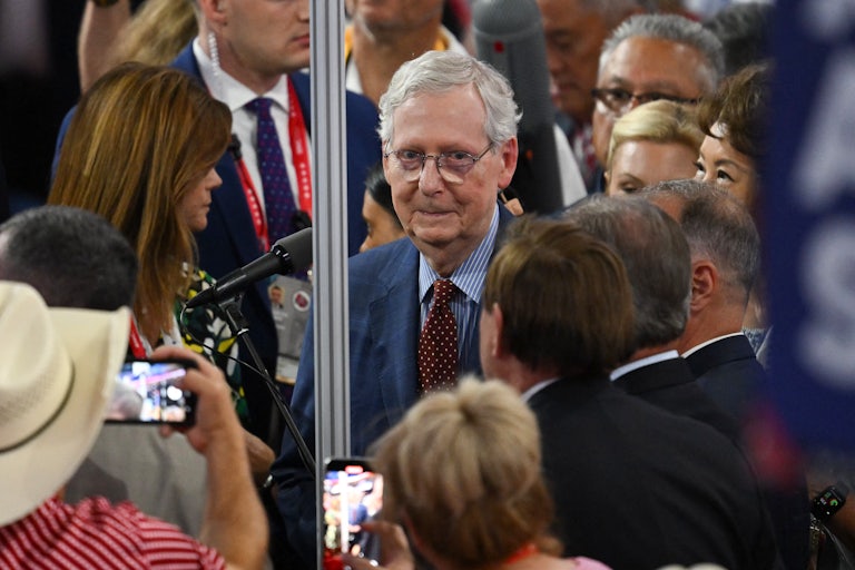 Mitch McConnell smiles among a crowd on the RNC floor. Others surround him with cameras.