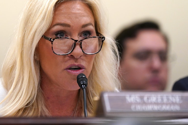 Representative Marjorie Taylor Greene speaks animatedly in a House hearing, her eyebrows raised.