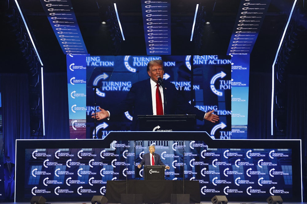 Donald Trump stands at a lectern while his image is projected above him.