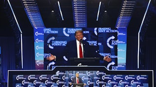 Donald Trump stands at a lectern while his image is projected above him.