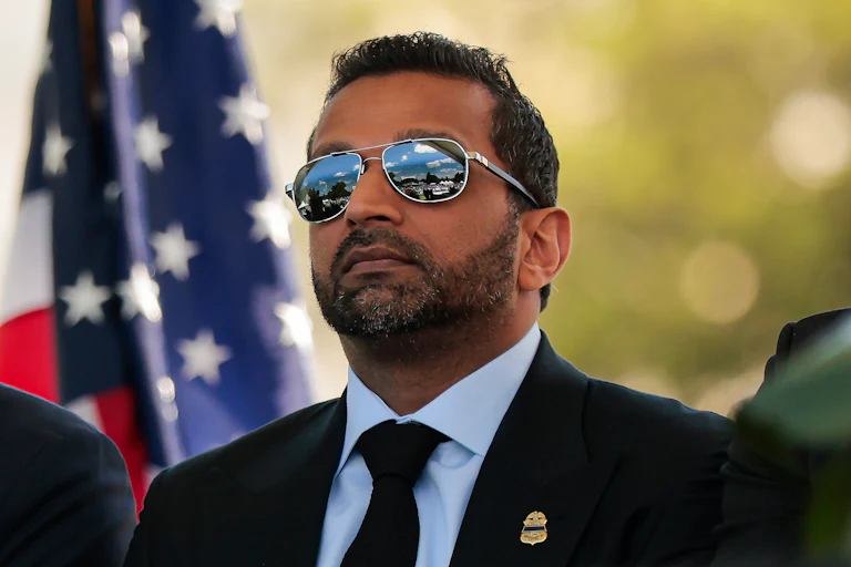 FBI Director Kash Patel wears large sunglasses and stands at an event