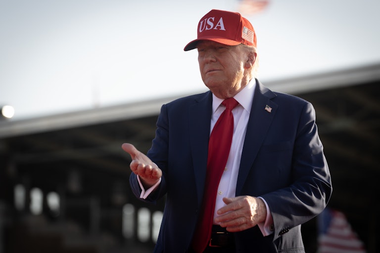 Donald Trump wears a red USA cap and smiles.