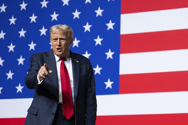 Donald Trump points and speaks while standing in front of a giant American flag