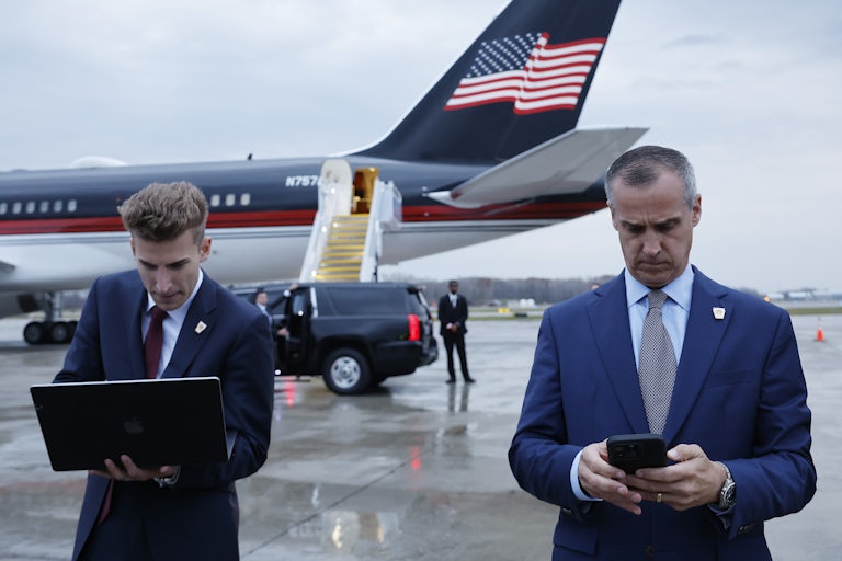 Corey Leandowski texts on his phone outside a plane with a U.S. flag on it.