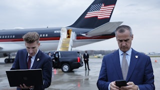 Corey Leandowski texts on his phone outside a plane with a U.S. flag on it.