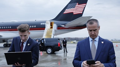 Corey Leandowski texts on his phone outside a plane with a U.S. flag on it.