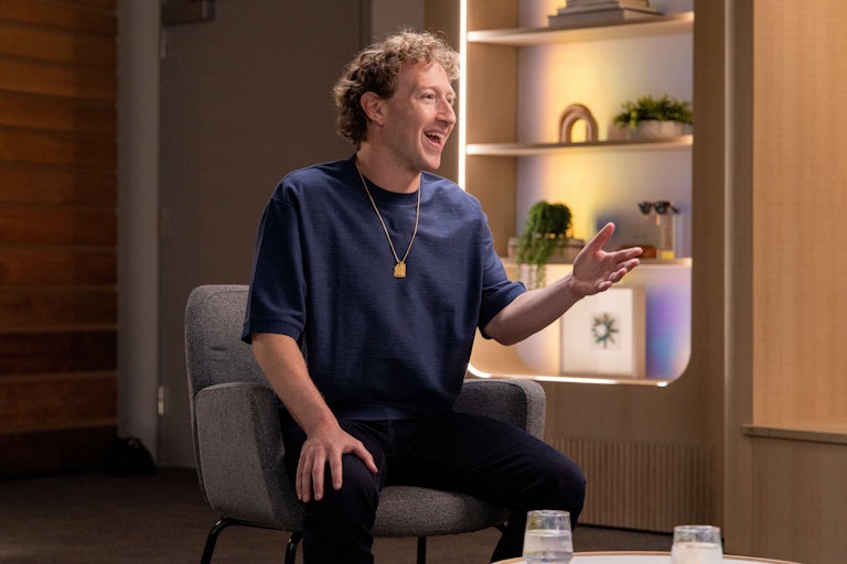 Mark Zuckerberg, seated, laughs and makes a hand gesture