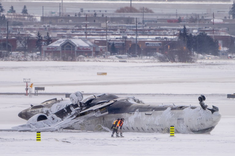 Workers survey a Delta Air Lines plane upside down and slightly crushed in the snow on the tarmac at Toronto Pearson International Airport.