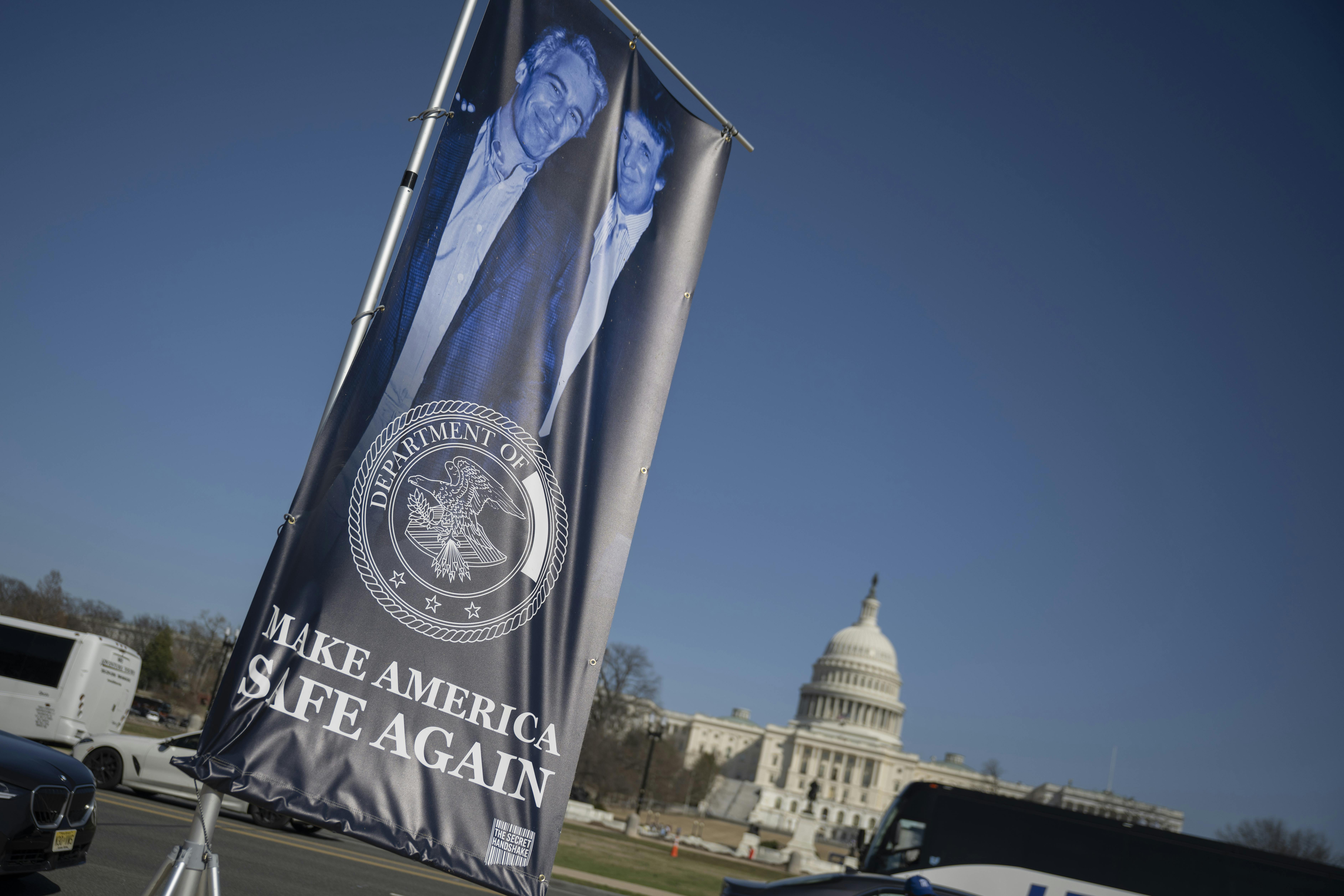 A banner of a photograph of Donald Trump and Jeffrey Epstein, emblazoned with the phrase, "Make America Safe Again," stands in front of the Capitol