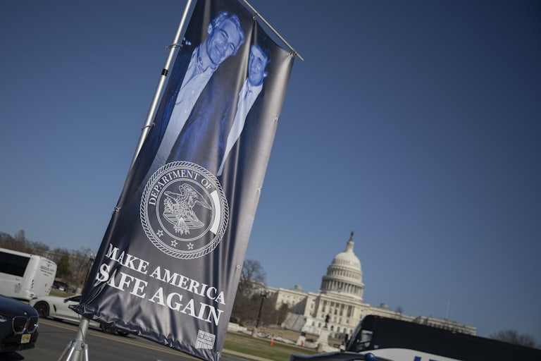 A banner of a photograph of Donald Trump and Jeffrey Epstein, emblazoned with the phrase, "Make America Safe Again," stands in front of the Capitol