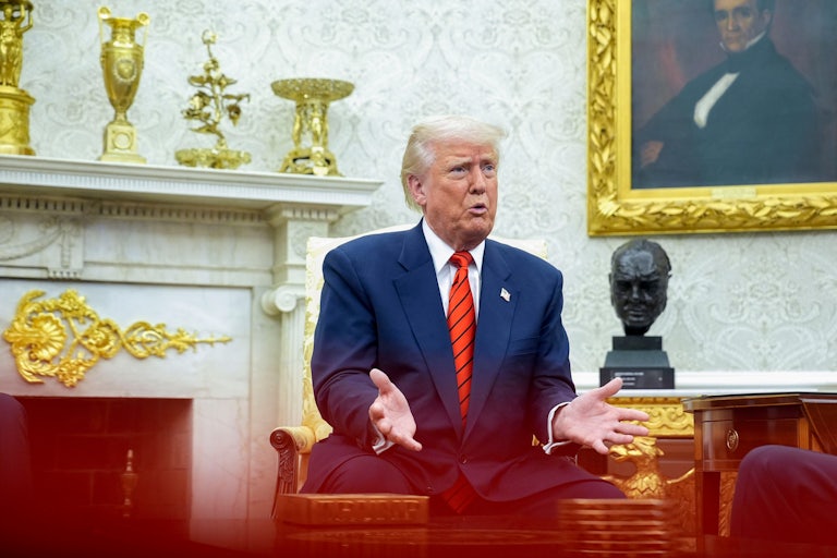 Donald Trump holds his hands out while speaking and sitting in the Oval Office