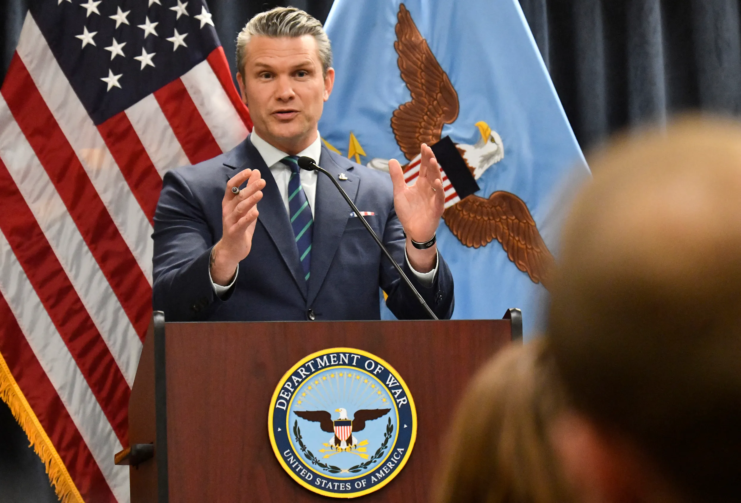 Defense Secretary Pete Hegseth gestures while speaking at a podium labeled "Department of War"