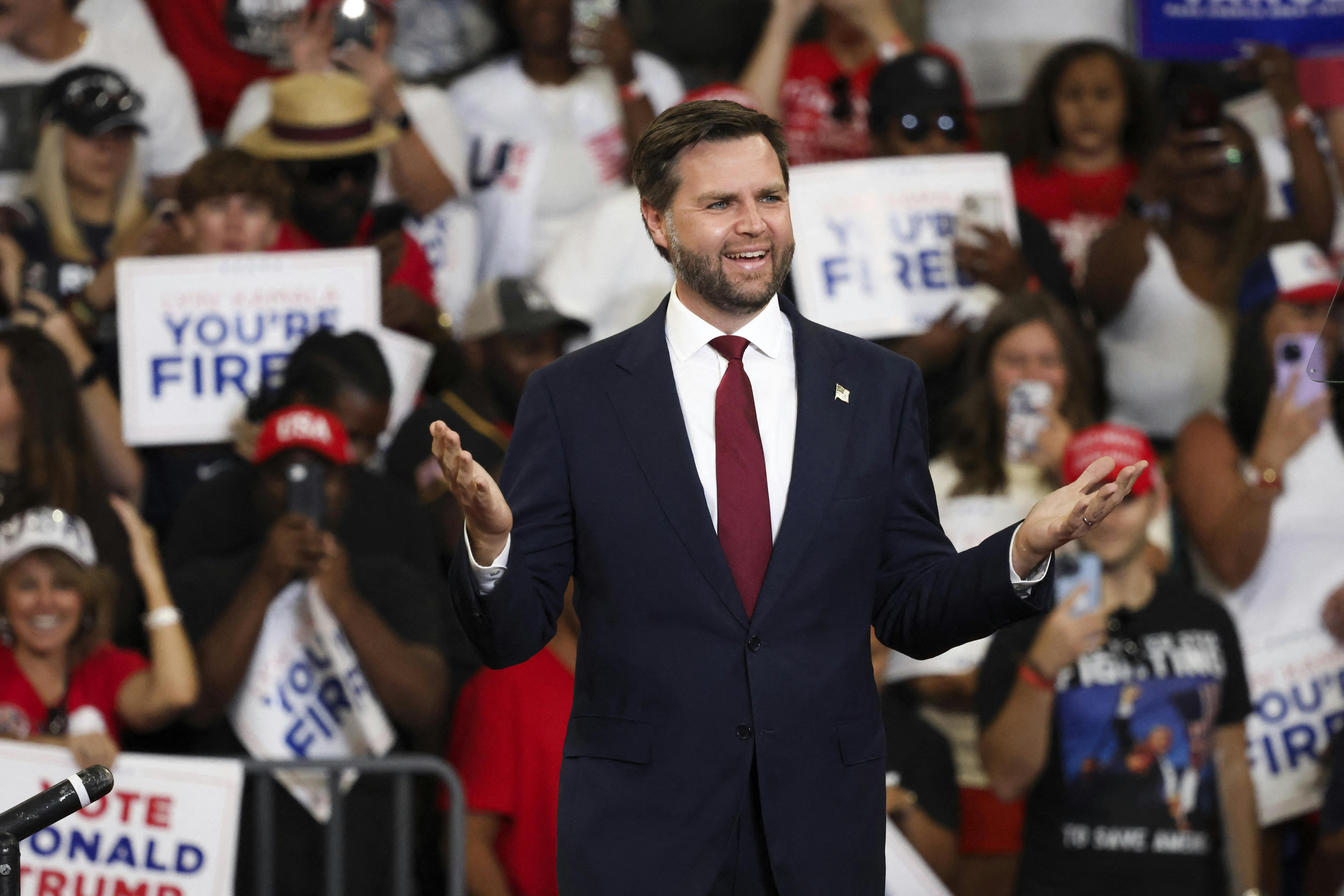 J.D. Vance smiles and holds his arms out as he stands in front of a crowd in Georgia holding signs reading "You're Fired."