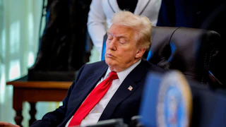Donald Trump, wearing a blue suit and red tie, sits in side profile on a black leather chair with his eyes closed. In front of him is a desk with an open binder.