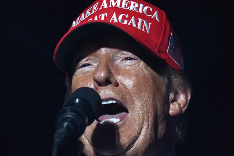 Donald Trump wears a Make America Great Again hat and speaks into a microphone