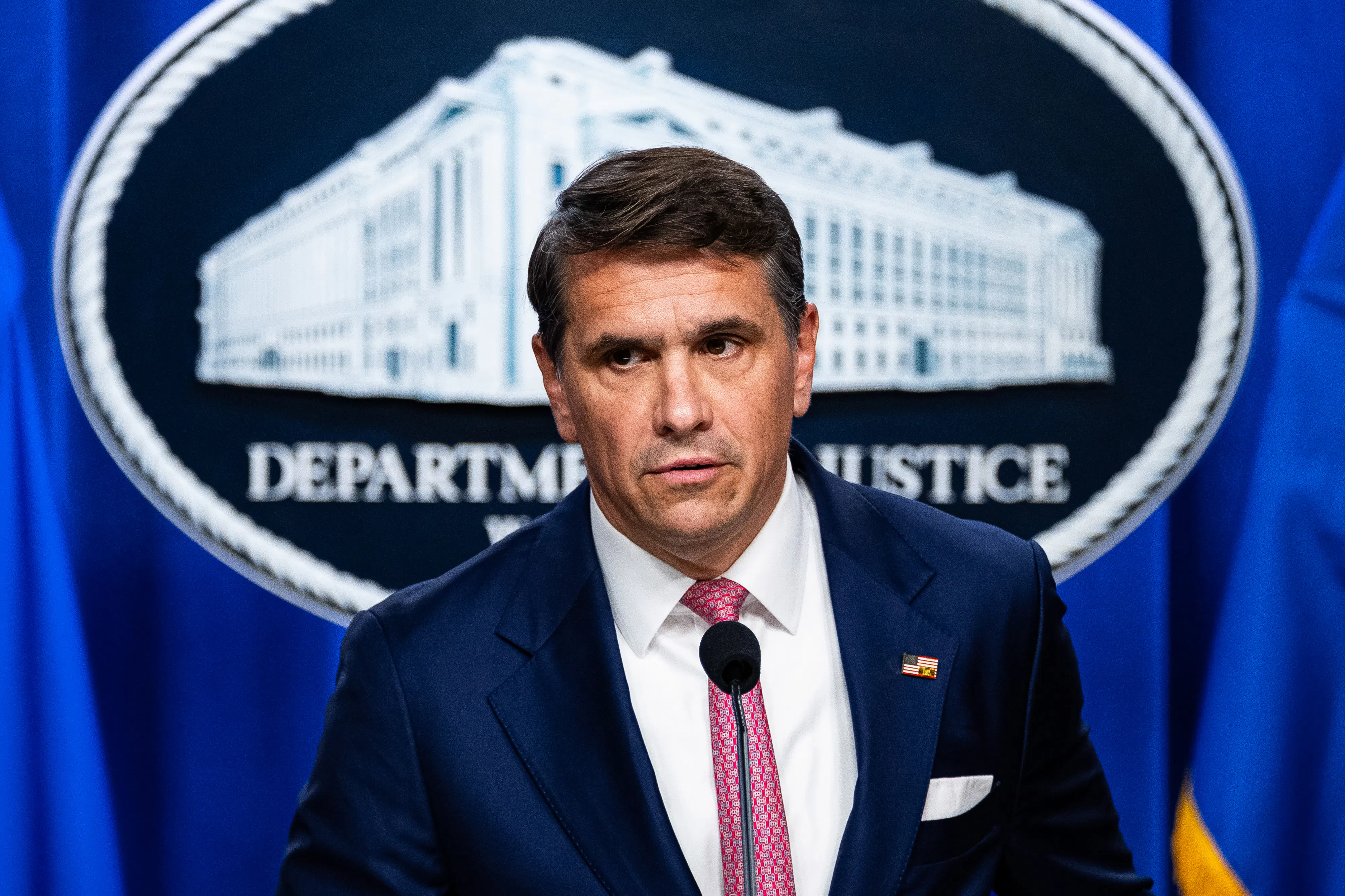 Acting Attorney General Todd Blanche stands in front of the Department of Justice logo