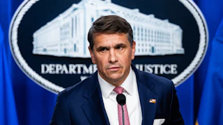 Acting Attorney General Todd Blanche stands in front of the Department of Justice logo