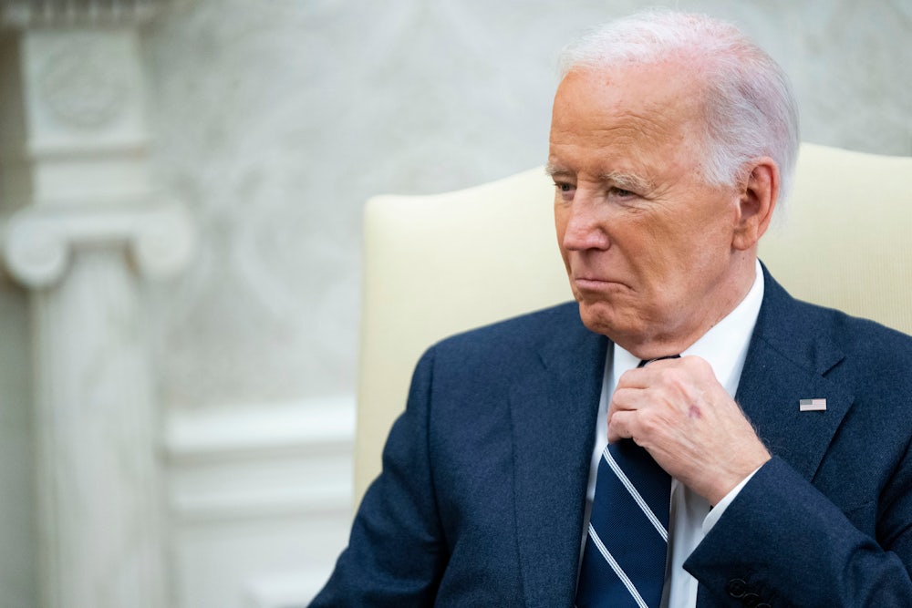 Joe Biden sits in a cream-colored chair in the Oval Office.